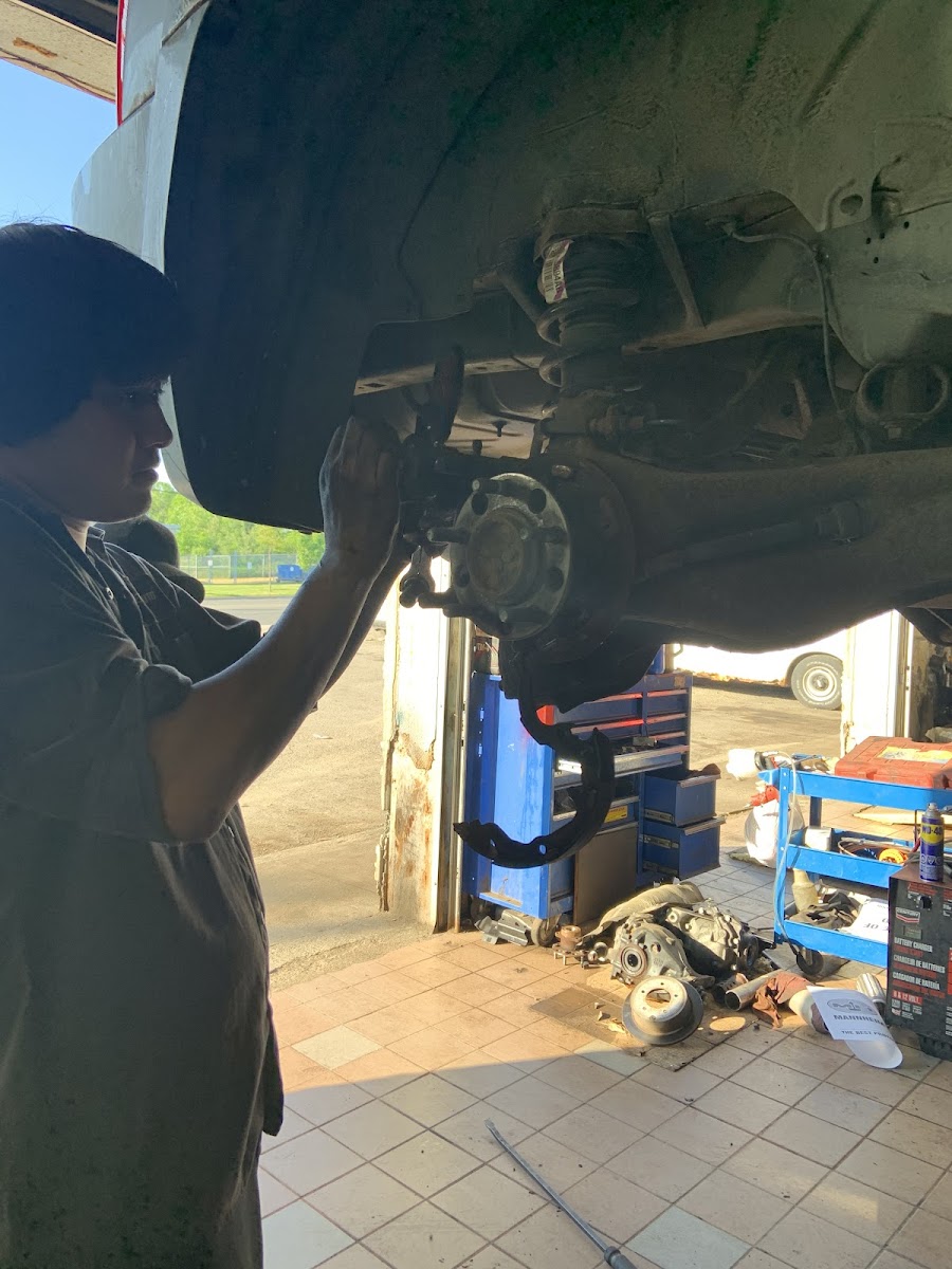 Mechanic working on a vehicle's front hub assembly under the lift